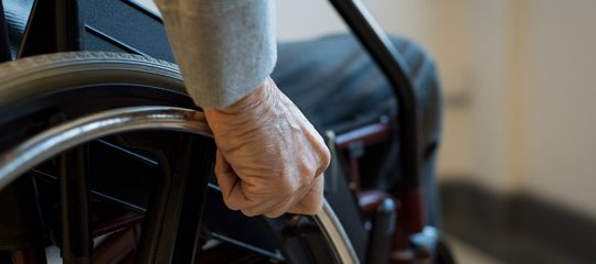 Senior on wheelchair Paralyzed old man using his wheelchair. Closeup of hand of disabled man pushing wheel of wheelchair. Detail of hand of senior man holding the wheel of wheelchair.