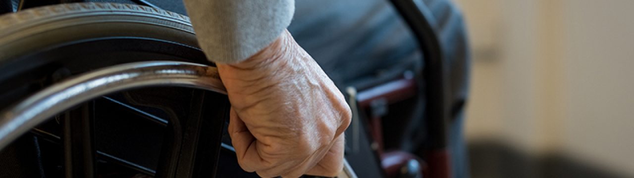 Paralyzed old man using his wheelchair. Closeup of hand of disabled man pushing wheel of wheelchair. Detail of hand of senior man holding the wheel of wheelchair.