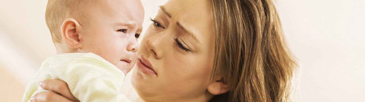 Young mother holding her baby boy who is crying.